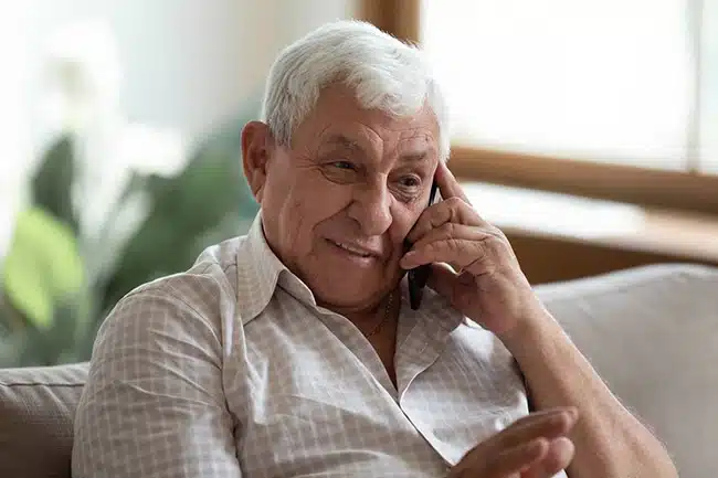 Un monsieur âgé sourit au téléphone, assis dans son canapé